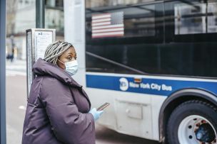 Ethnic doctor with smartphone against urban bus