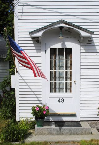 American flag waving near door of white residential house